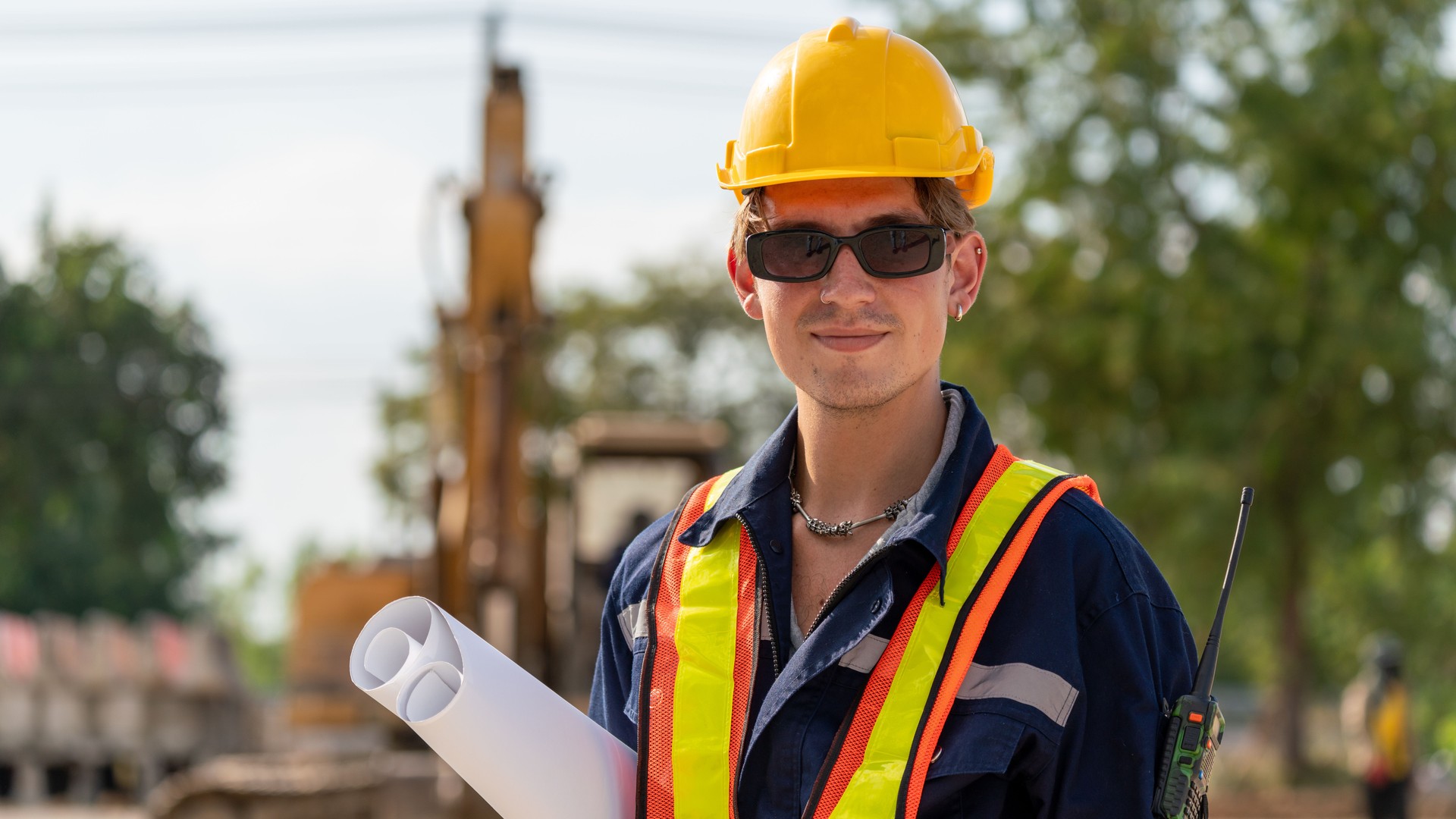 Szkolenie budowlane A-KWADRAT Klaudia Kaczmarek. Uczestnik w kamizelce odblaskowej trzyma plany konstrukcyjne na placu budowy